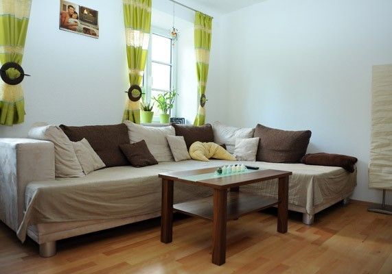 Gemütliches Wohnzimmer mit Couch, Holzboden und grünen Vorhängen.